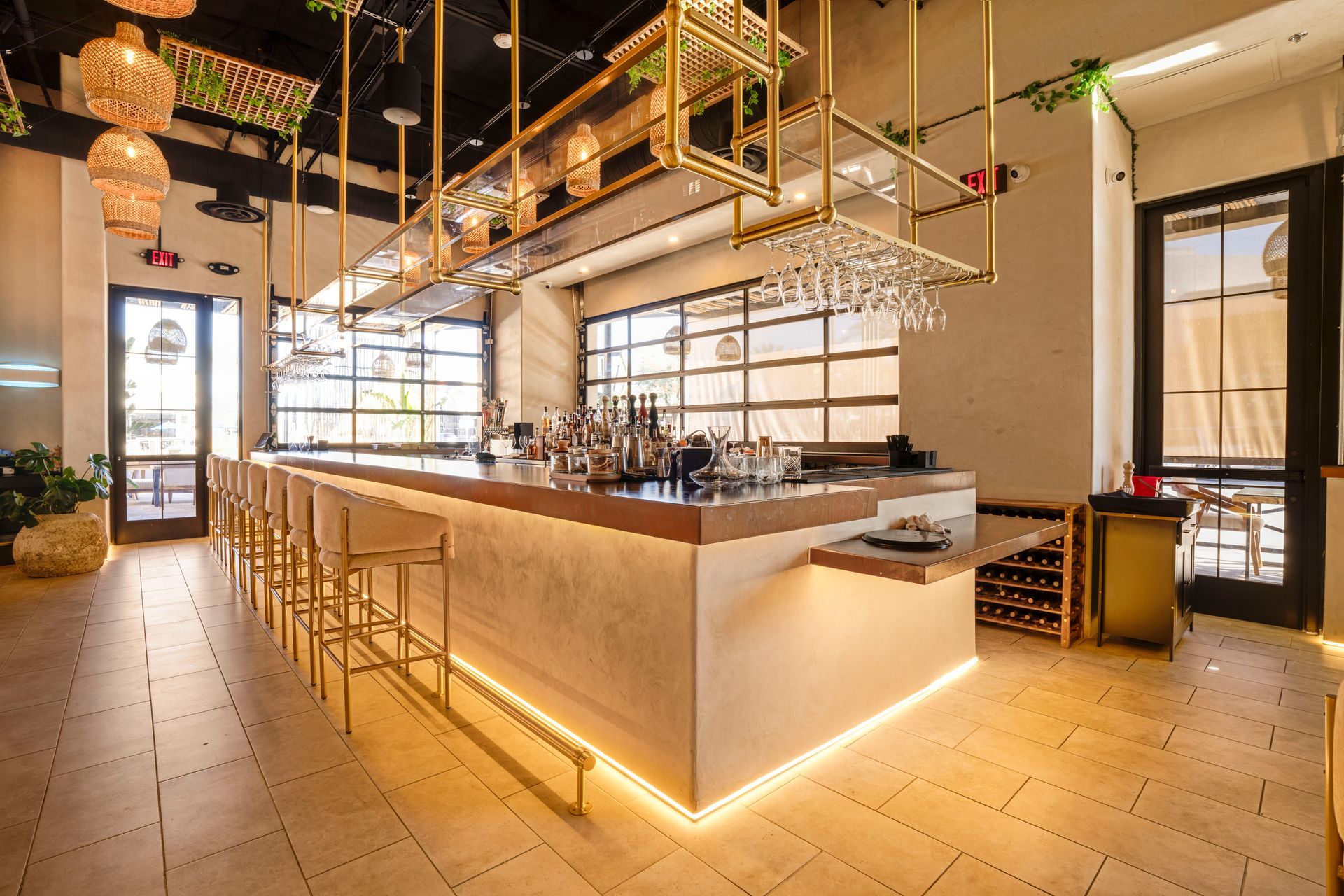 Modern restaurant interior with a lit bar, high stools, hanging plants, and warm ambient lighting