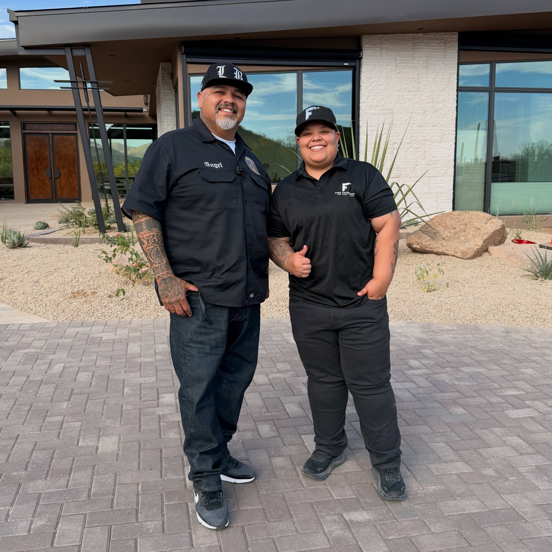 Two people in black uniforms smiling outside a building with a glass entrance.