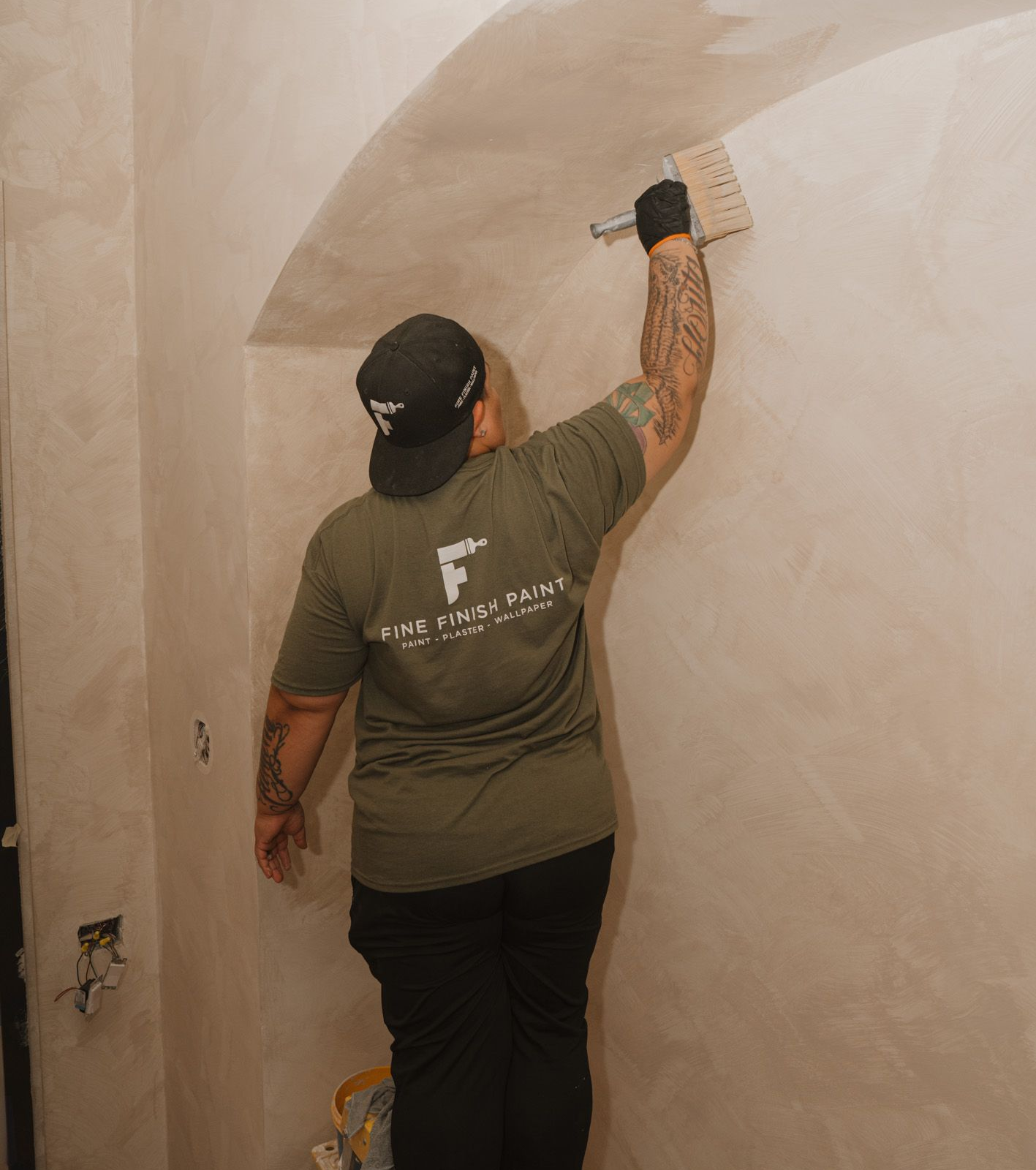 Person plastering a beige wall with a trowel in an unfinished room