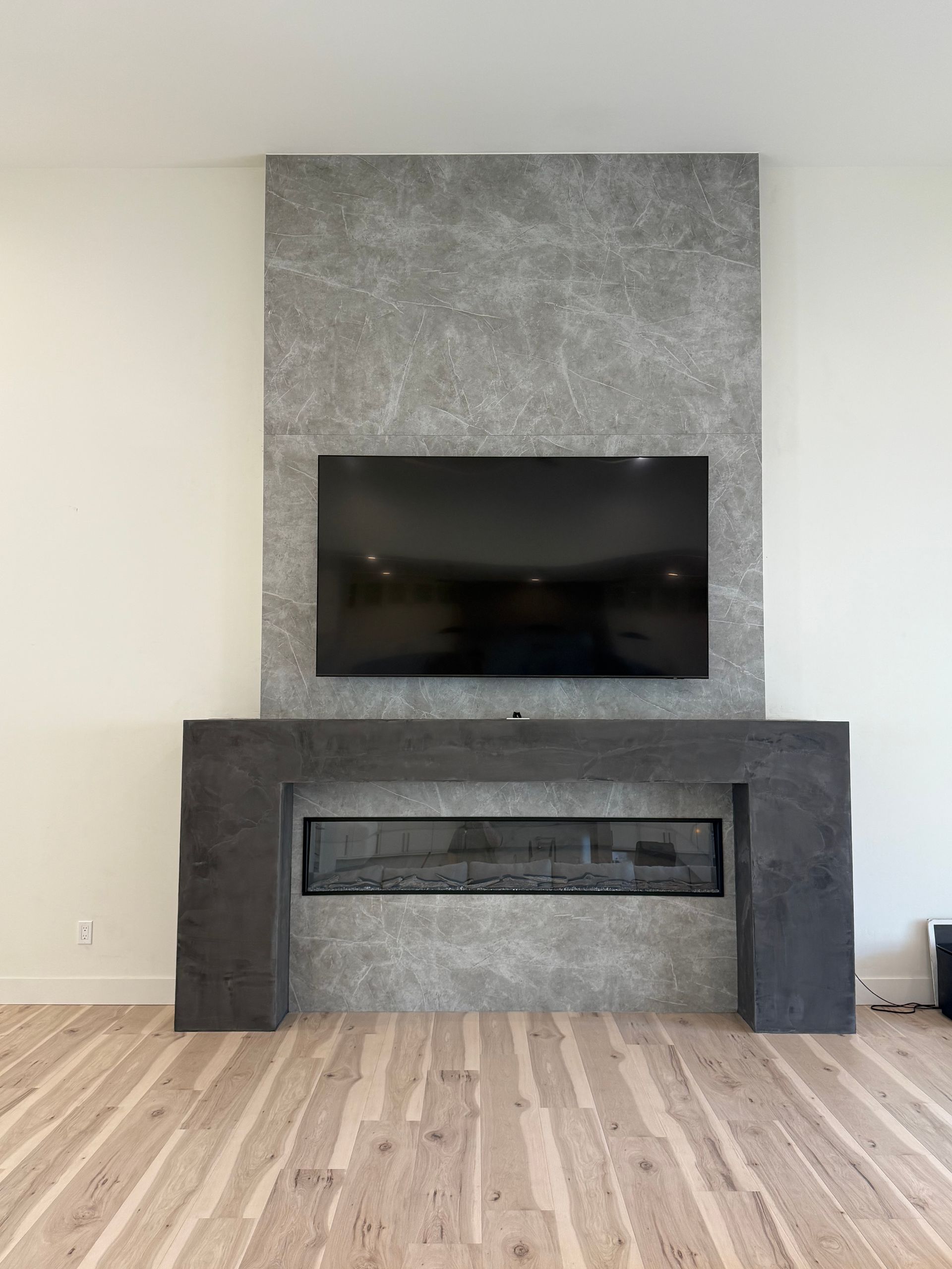 Modern living room with a wall-mounted TV above a dark stone fireplace and light wood floors.