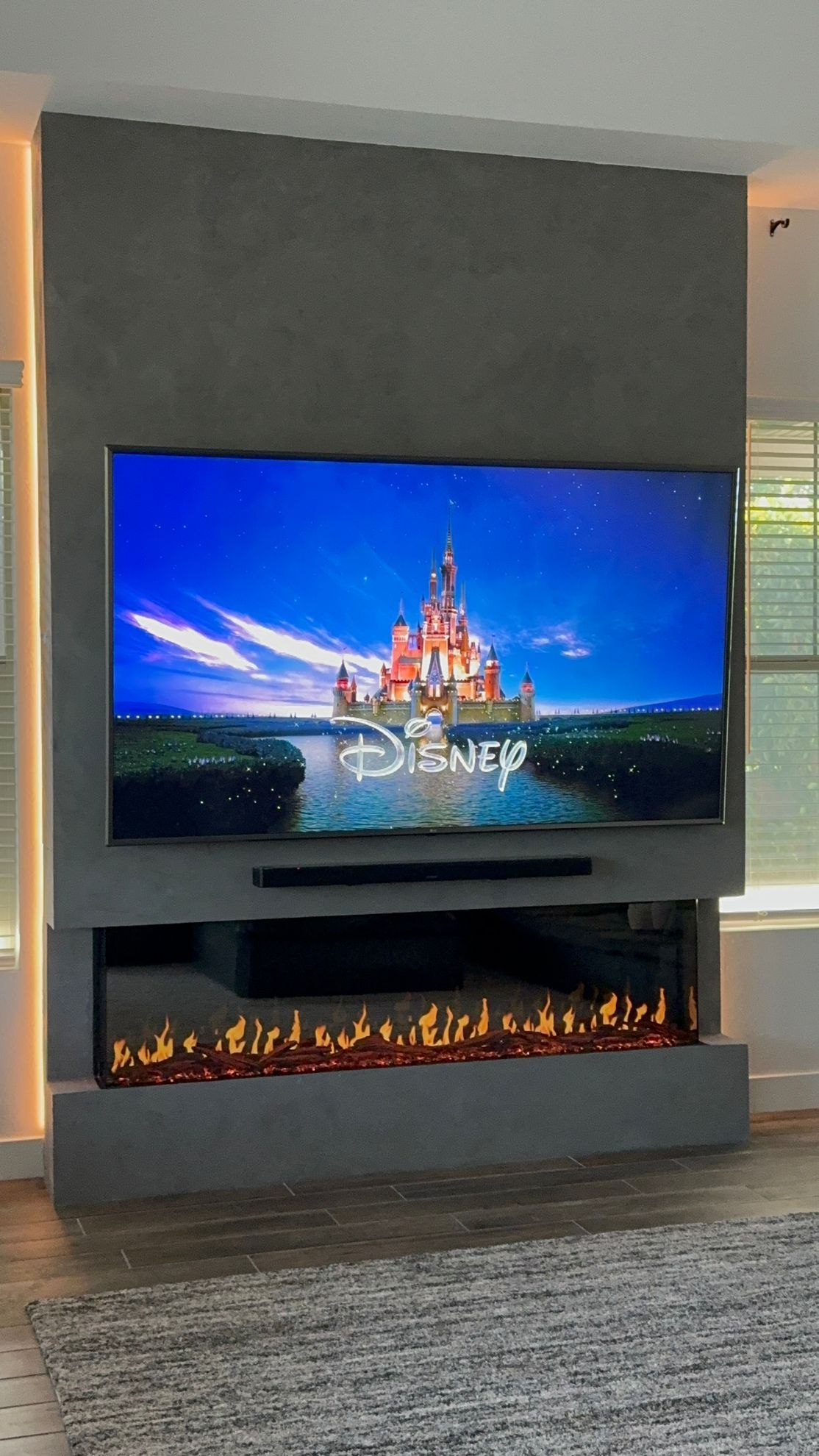 Flat-screen TV above a modern electric fireplace in a living room, showing the Disney castle splash screen.
