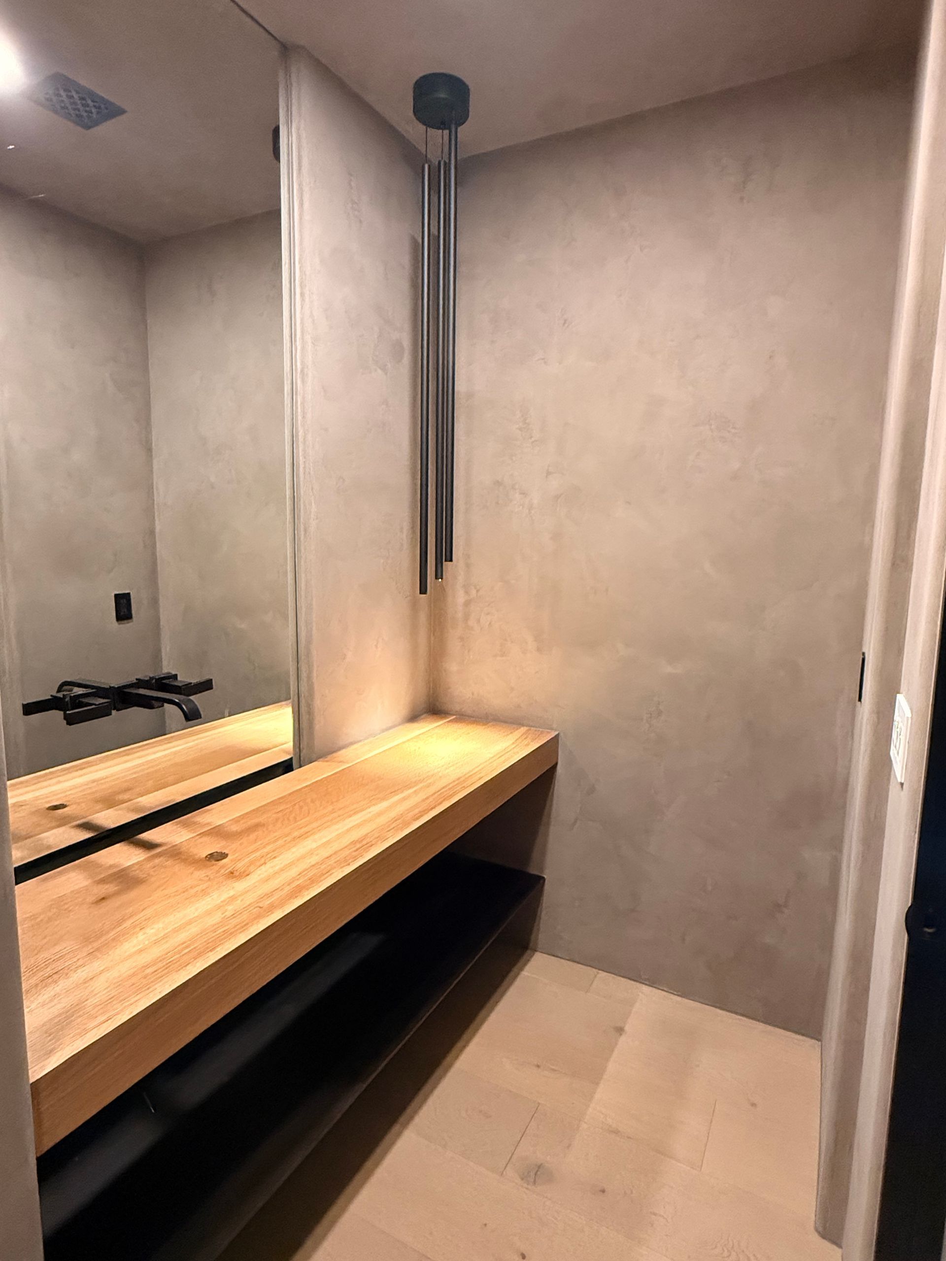Modern bathroom vanity with wooden countertop, mirror, beige walls, and hanging black towel rail.