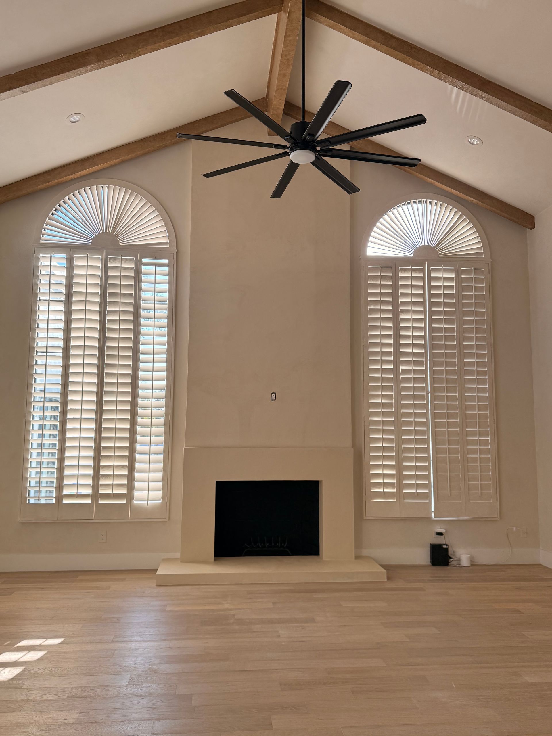 Bright living room with tall arched windows, shutters, fireplace, and a ceiling fan.