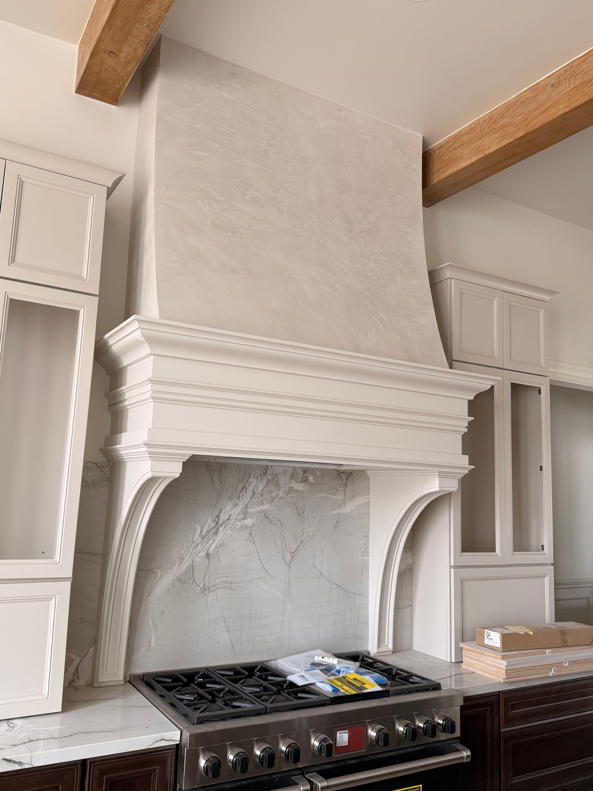 Modern kitchen with large plaster range hood, white cabinets, and a stainless steel stove top