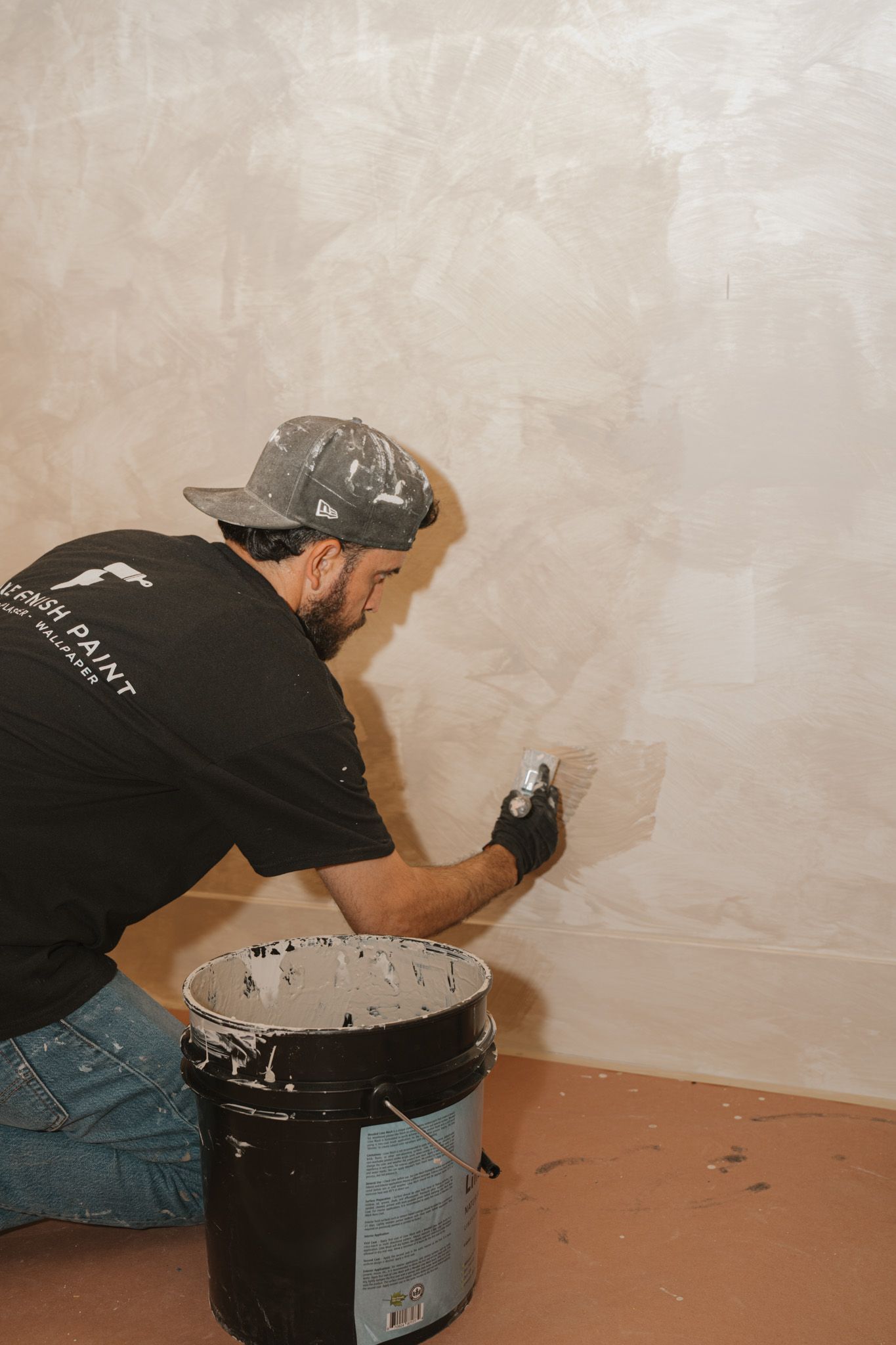 Person applying white paint to a wall with a roller beside a paint bucket