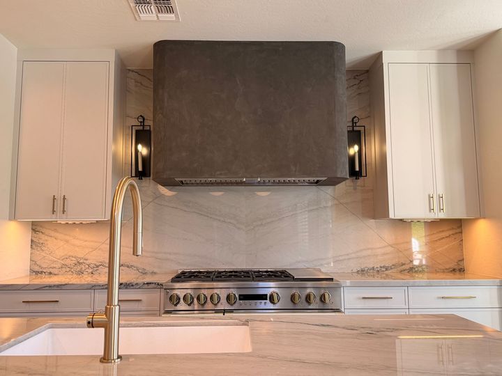 Modern kitchen with white cabinets, stainless range, and marble backsplash beneath a large black hood