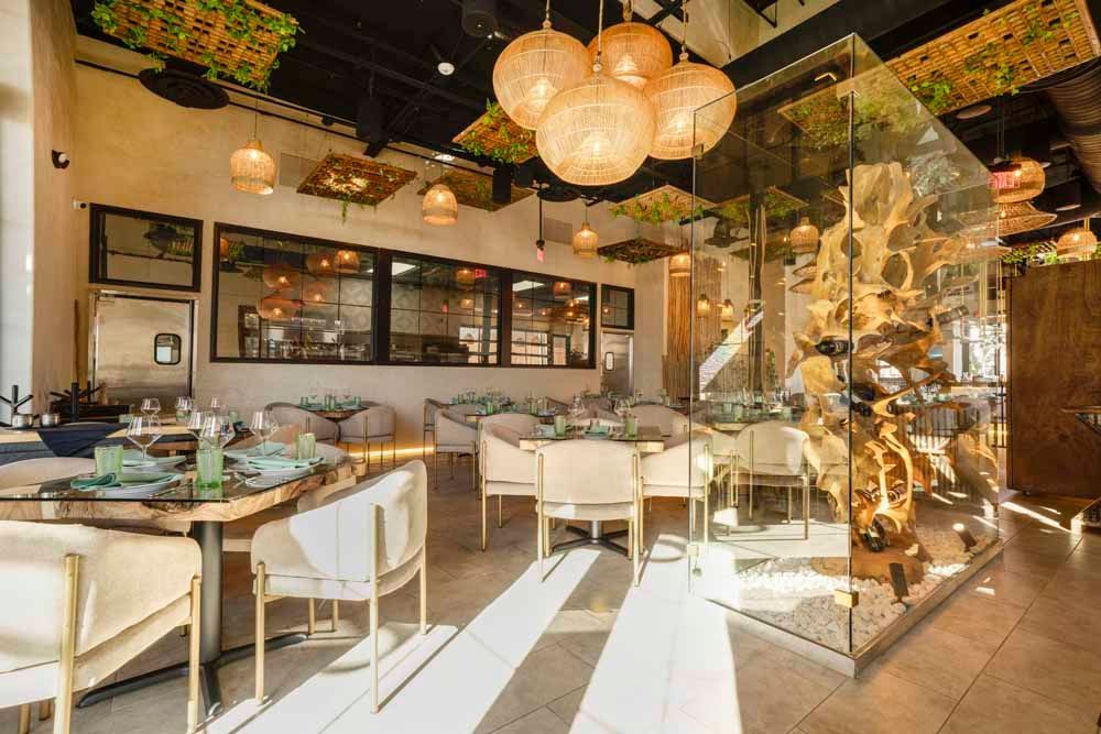 Elegant restaurant dining room with white chairs, round tables, warm pendant lights, and glass decor