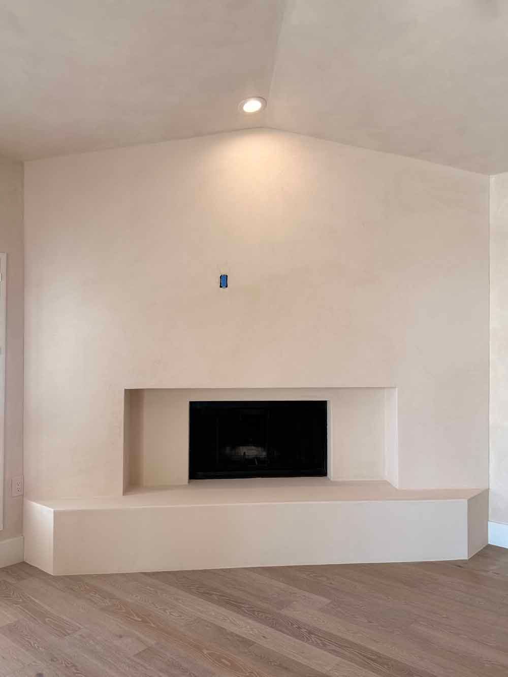 Empty white living room with a built-in fireplace and recessed alcove beneath a sloped ceiling.
