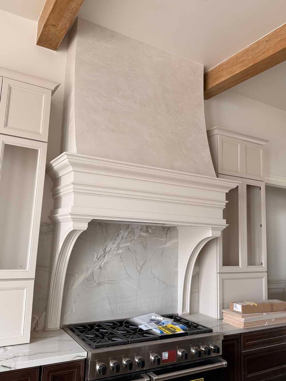 White kitchen with a large decorative stucco fireplace above a stainless steel stove and two tall cabinets.