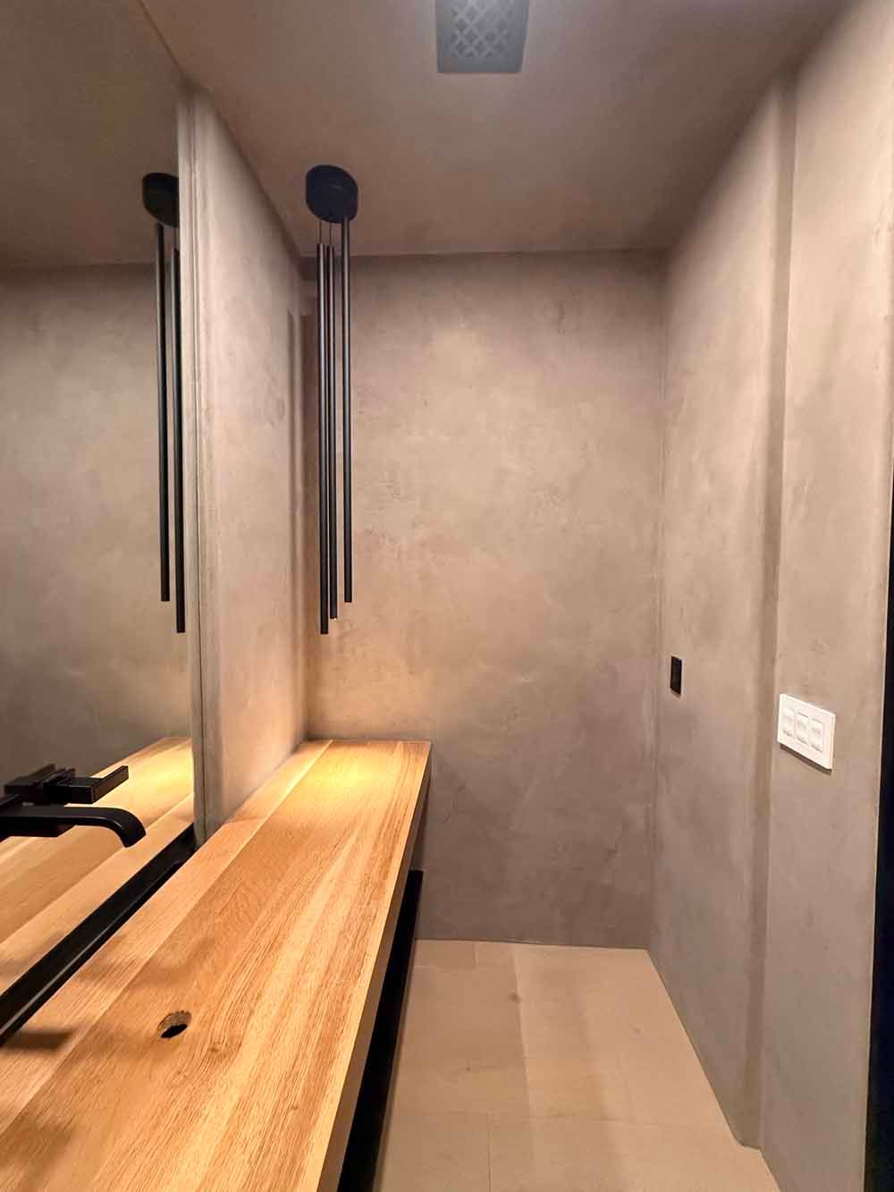 Minimalist locker room bench area with mirrors, wooden bench, gray walls, and hanging black hooks.