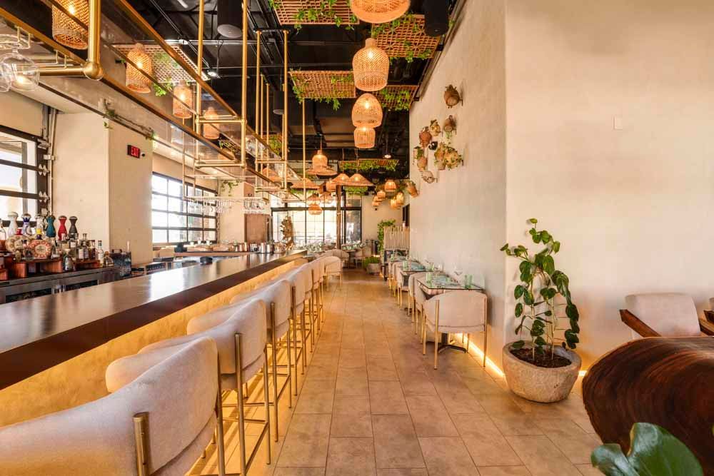Stylish bar interior with long counter, hanging lanterns, plants, and warm ambient lighting