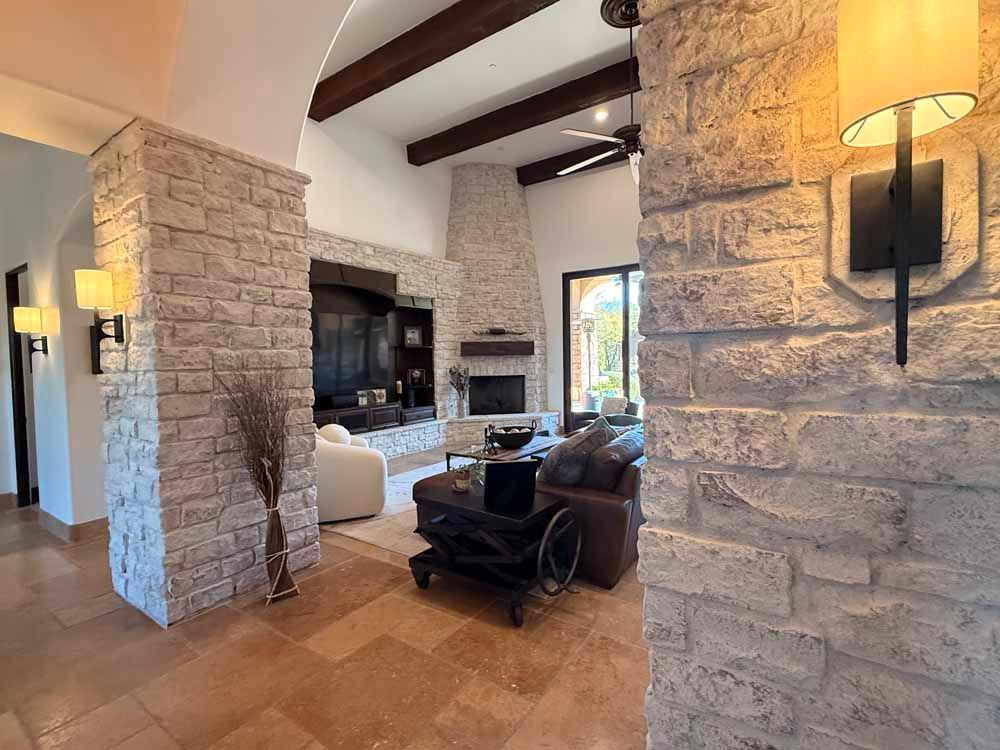 Stone living room with exposed beams, fireplace, and leather chairs around a seating area.