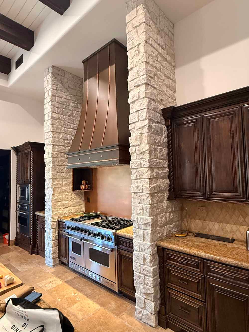 Modern kitchen with stone pillar, wood cabinetry, stainless range, and copper range hood