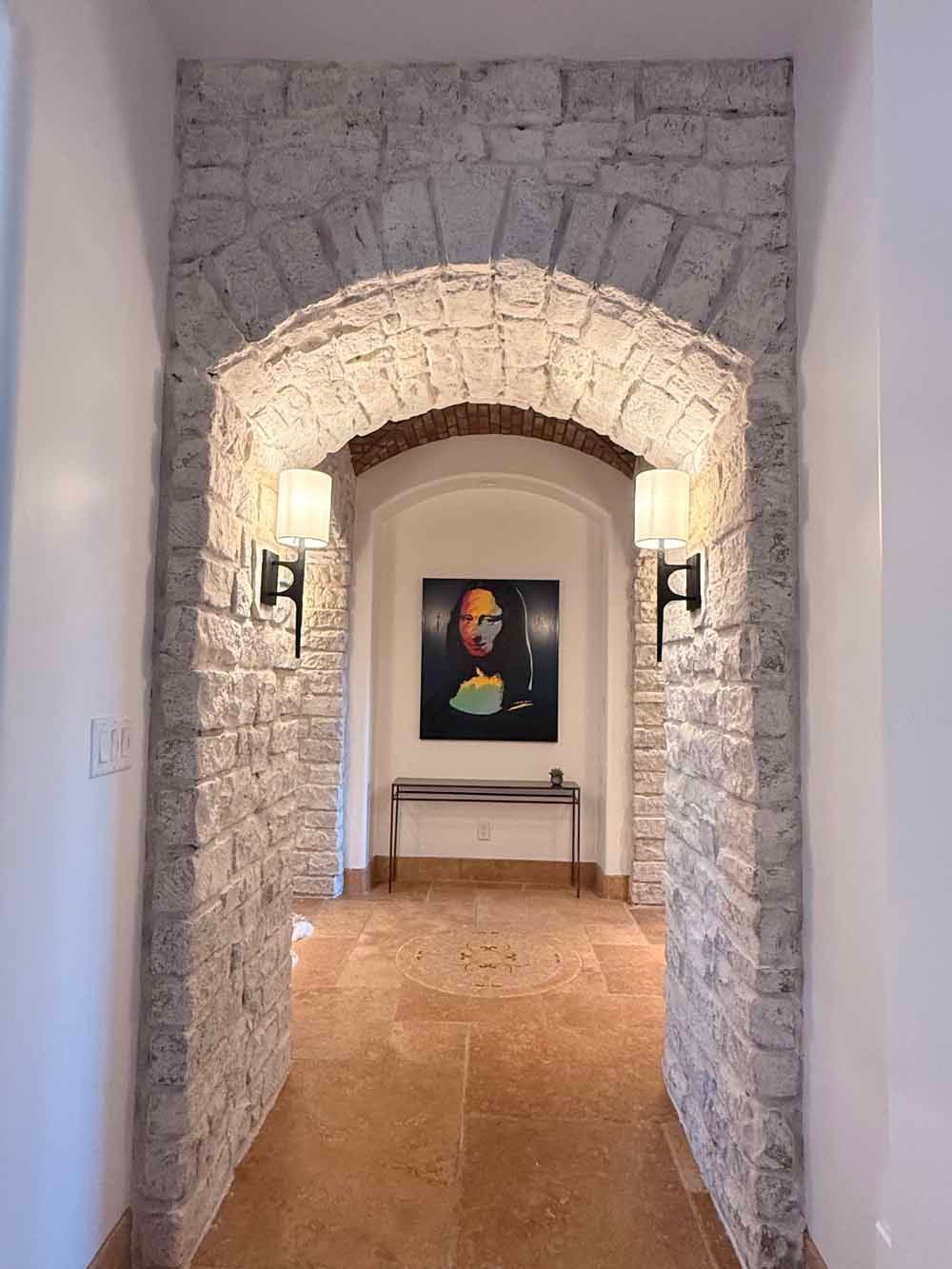 Stone hallway archway leading to a framed portrait on a wall in a softly lit interior
