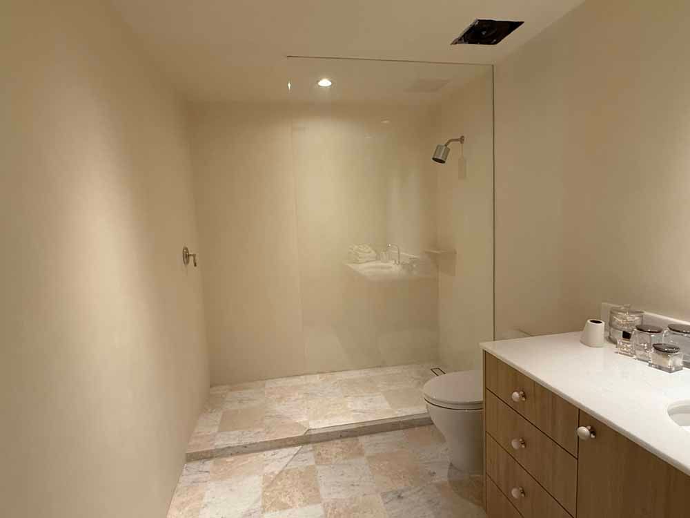Empty beige bathroom with a large walk-in shower, toilet, and vanity with drawers.