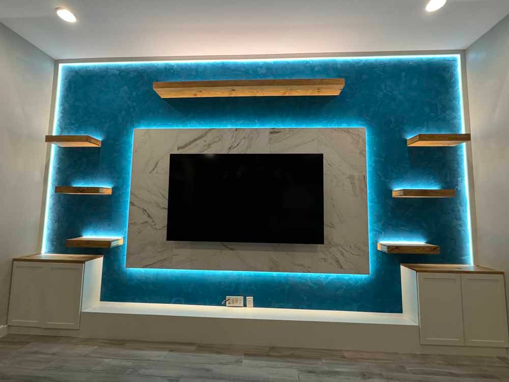 Modern living room wall with a wall-mounted TV, blue LED backlighting, and floating shelves.