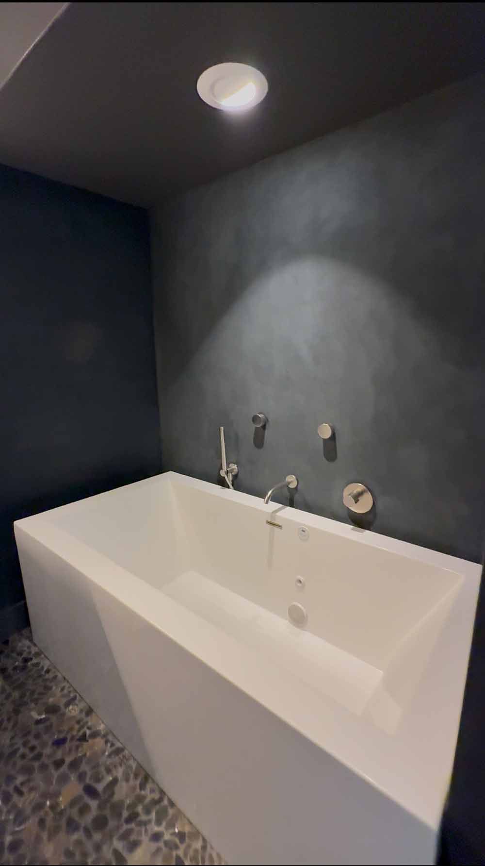 Modern bathroom with a white freestanding tub, dark walls, and pebble tile flooring.