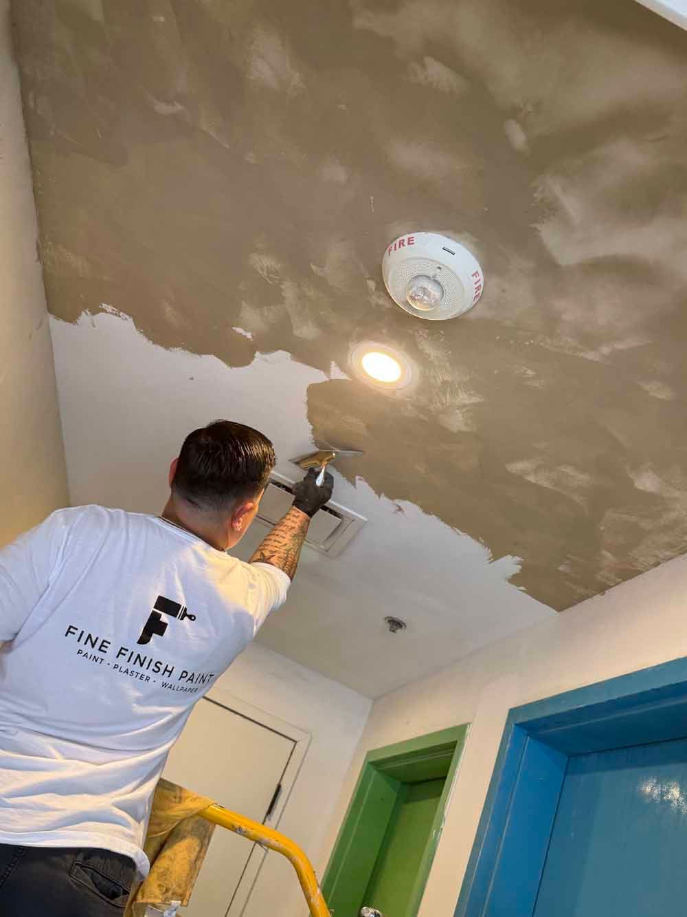 Worker painting a ceiling with a spray gun in a room with green and blue doors