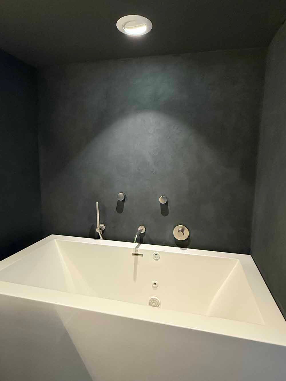 Modern bathroom with a white soaking tub, dark gray walls, and a ceiling light above the faucet area