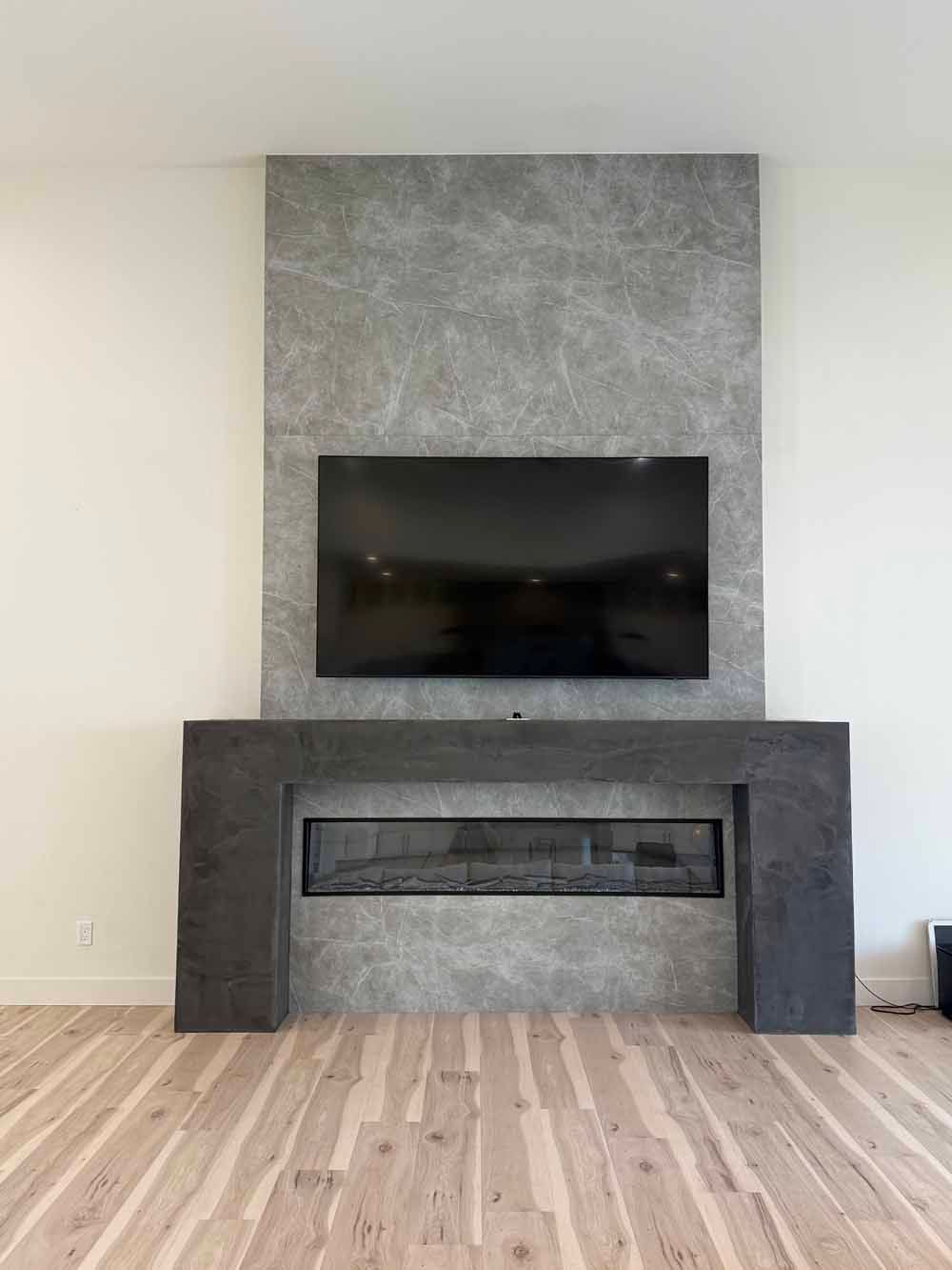 Modern living room with a wall-mounted TV above a dark fireplace and gray stone surround