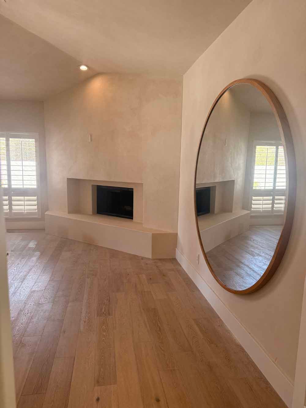 Bright living room with hardwood floors, a fireplace, and a large round wall mirror.