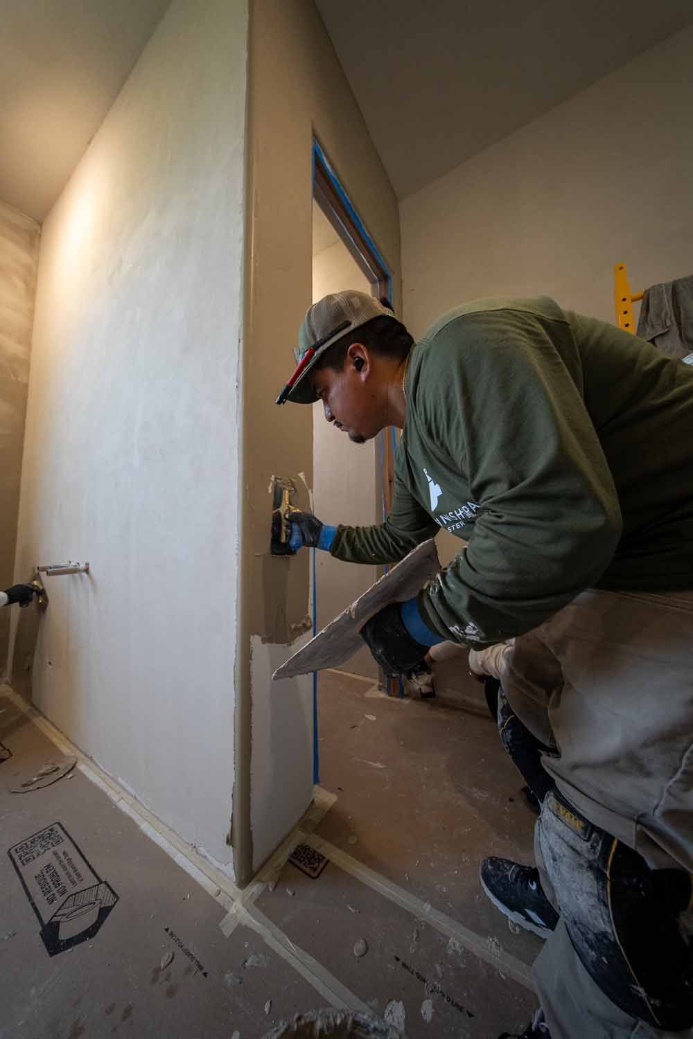 Worker installing drywall in a hallway, using a trowel on a wall corner.