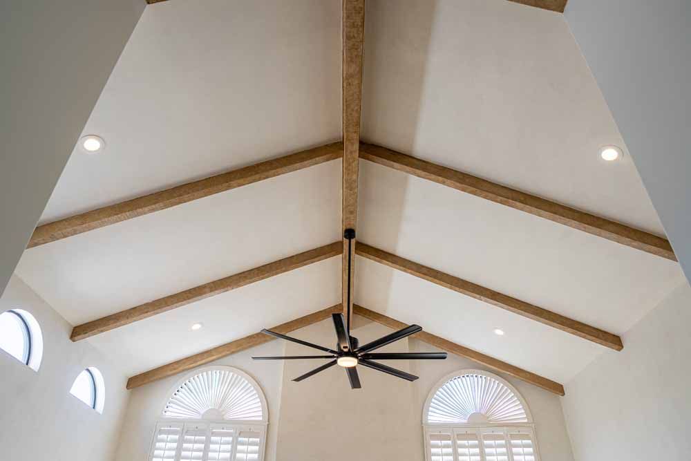 Cathedral-style vaulted ceiling with exposed wood beams, a ceiling fan, and arched windows above shutters