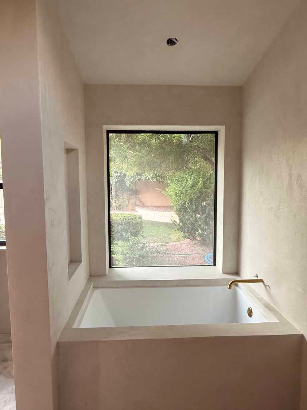 Modern bathroom with a white soaking tub beside a large window overlooking greenery.