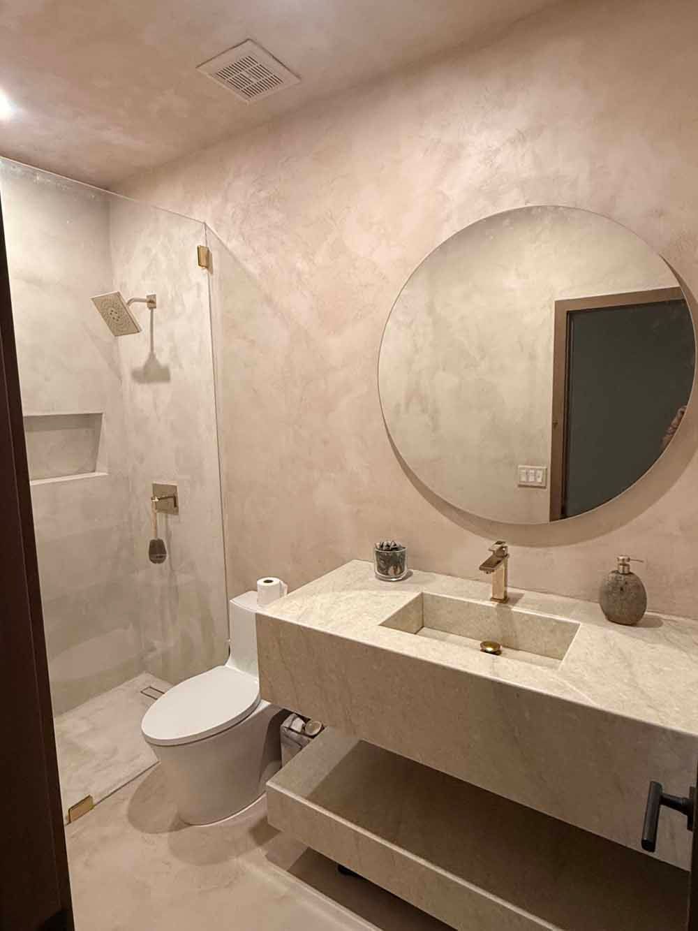 Modern beige bathroom with shower, toilet, and vanity with round mirror