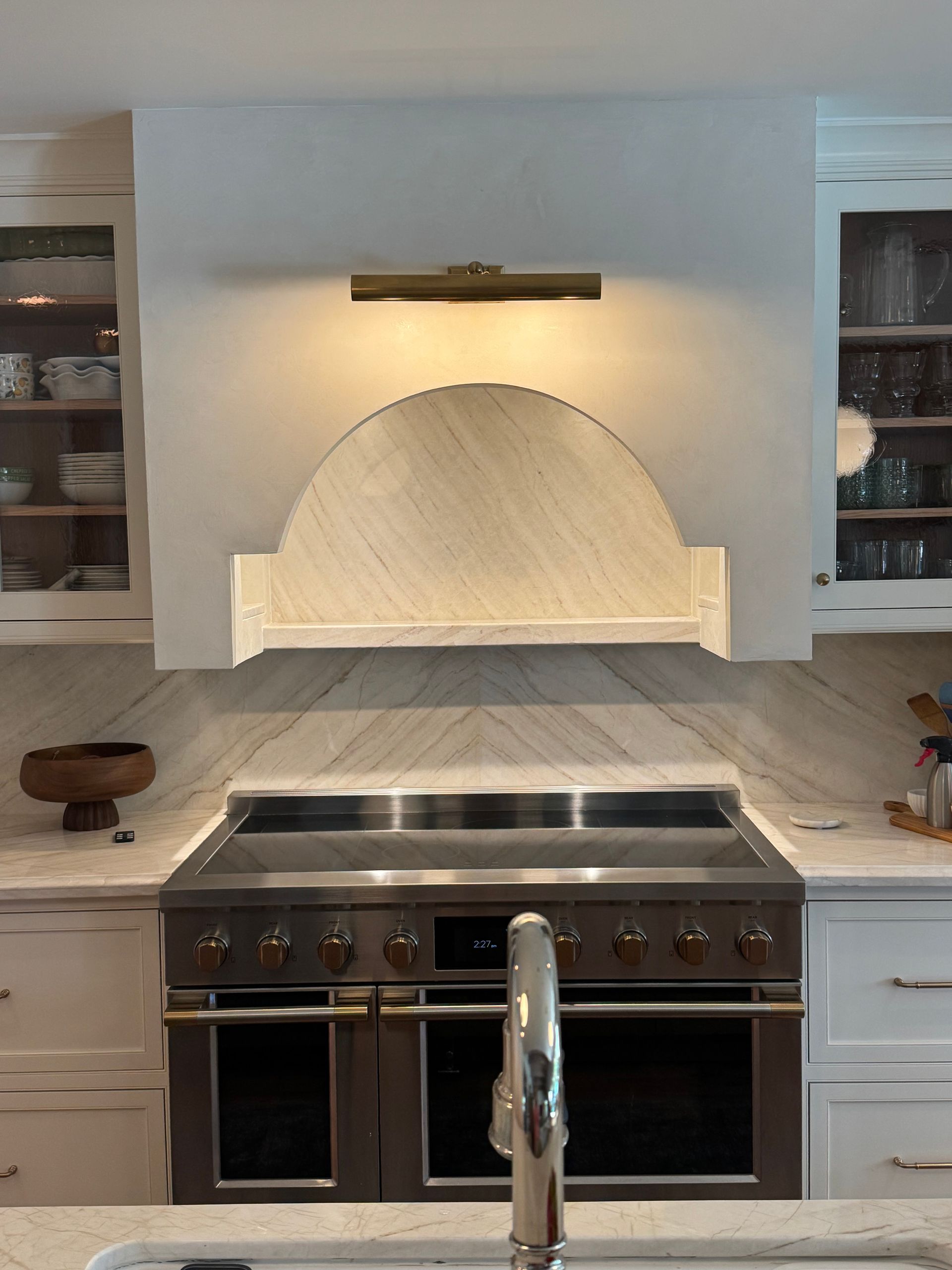 Modern kitchen with stainless-steel range, marble backsplash, and lit arched niche above the stove.