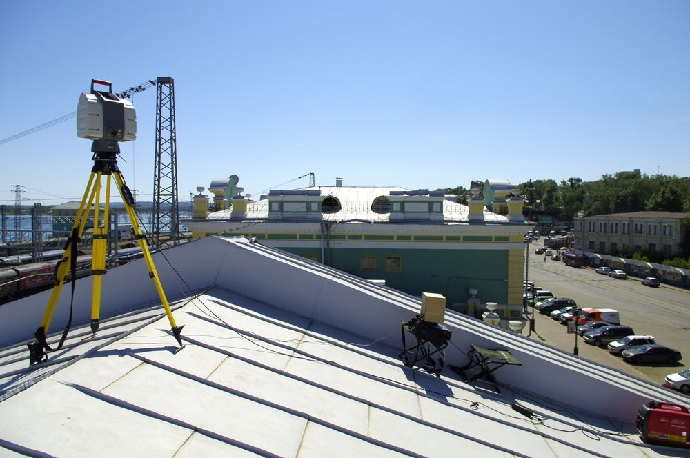 Surveying equipment on a rooftop overlooking a parking lot and buildings on a sunny day