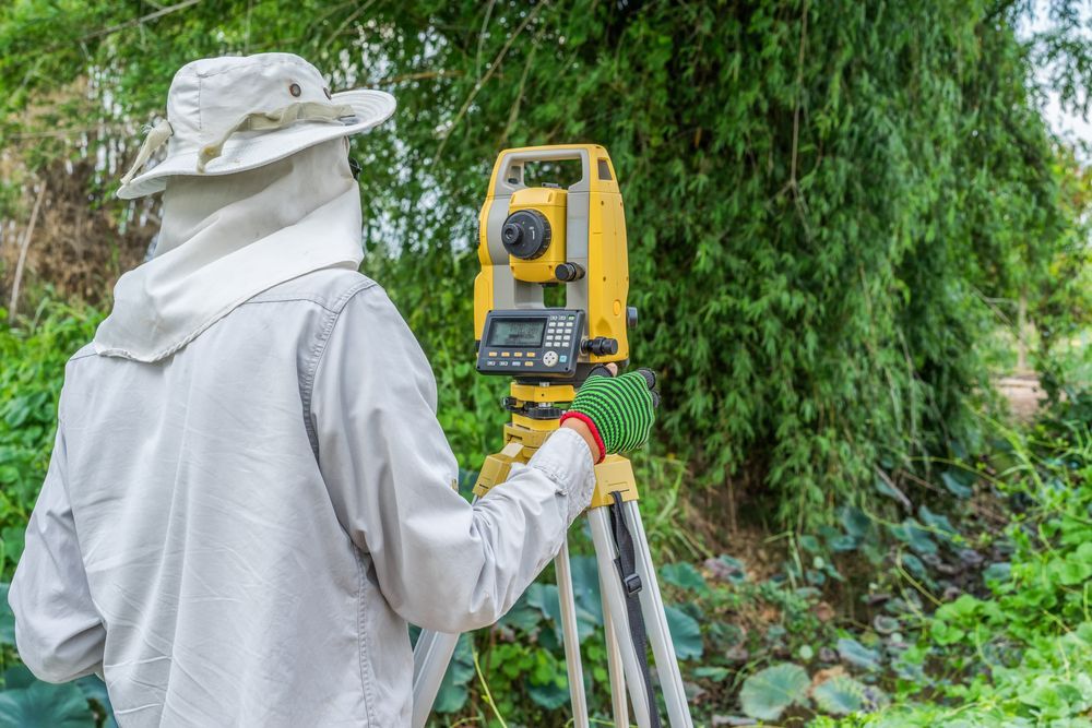 Surveyor using a yellow total station on a tripod in a lush outdoor area