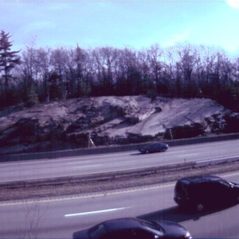 Cars on a highway beside a rocky embankment and leafless trees under a blue sky