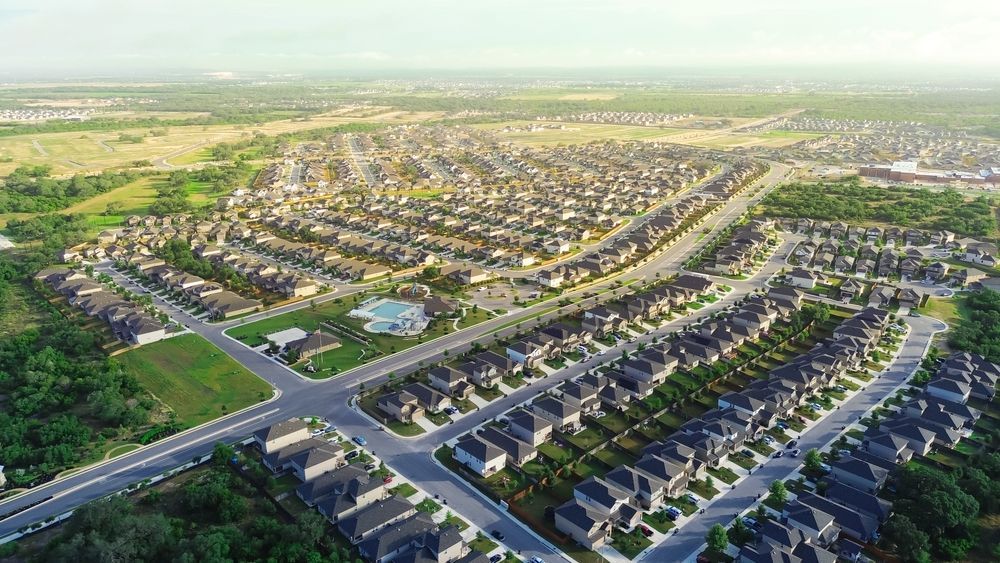 Aerial view of a large suburban housing development with curving streets and green open land beyond