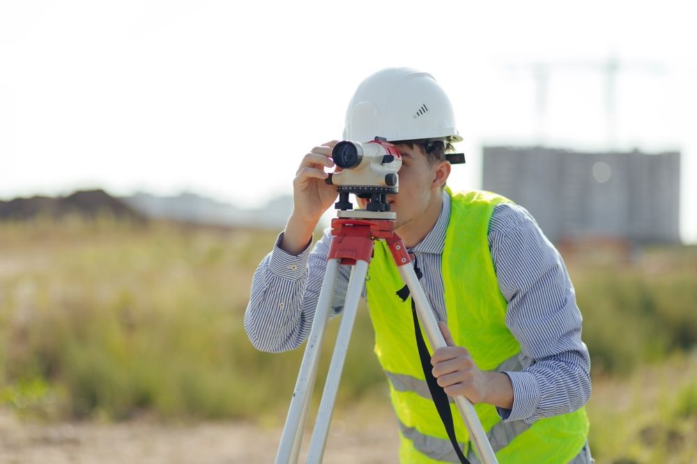 Surveyor in white hard hat and neon vest using a tripod-mounted instrument outdoors