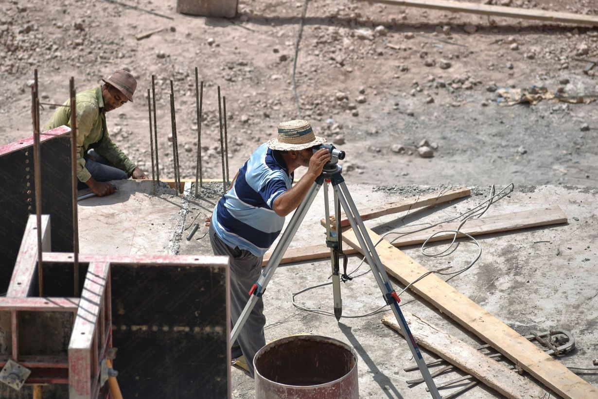 Construction workers pouring concrete using a tripod and hose at a building site