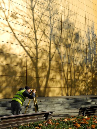 Worker using a tripod on train tracks beside a gold reflective building wall