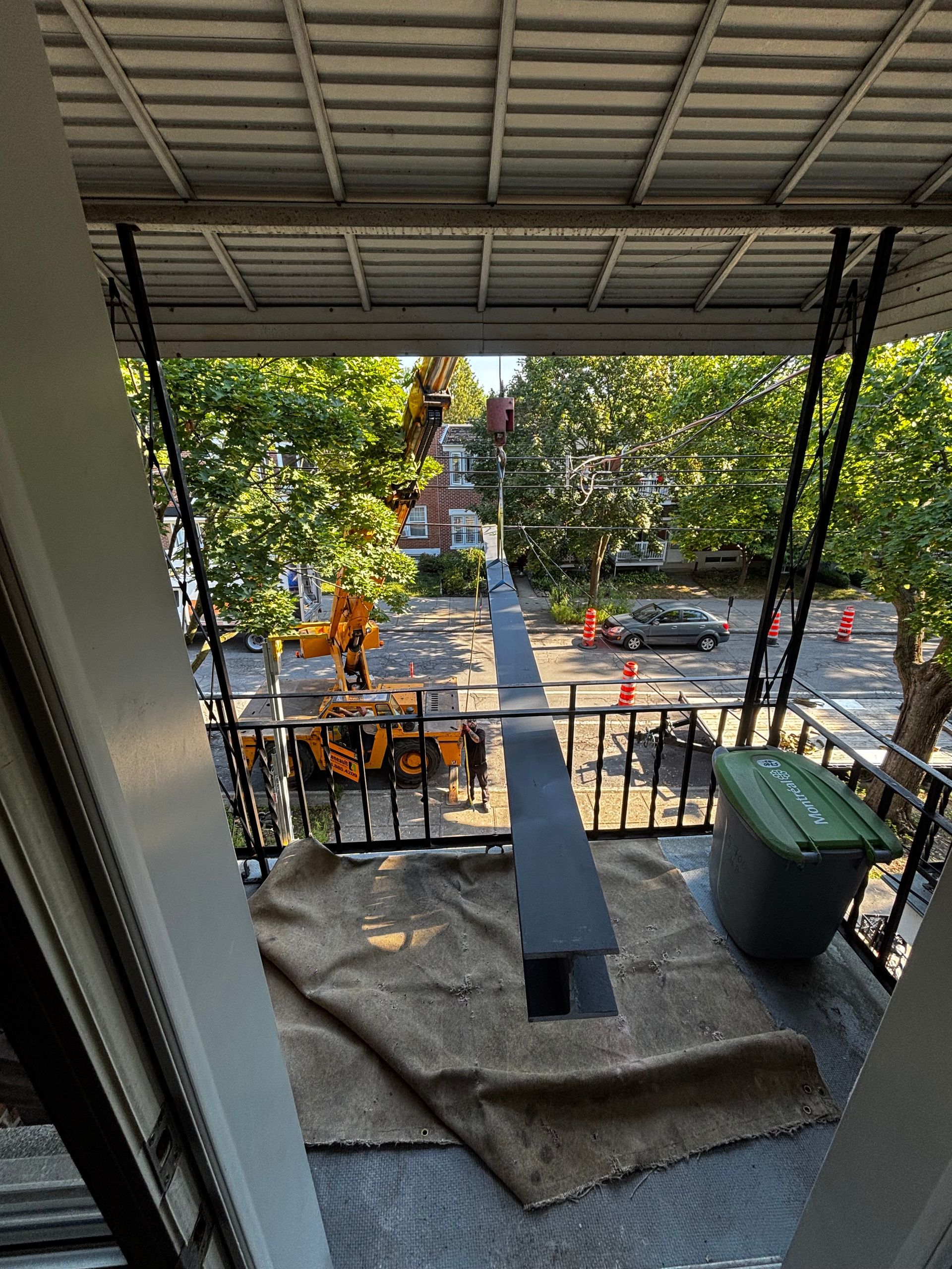 Vue depuis un balcon d'une rue avec des engins de chantier, des arbres et des voitures.