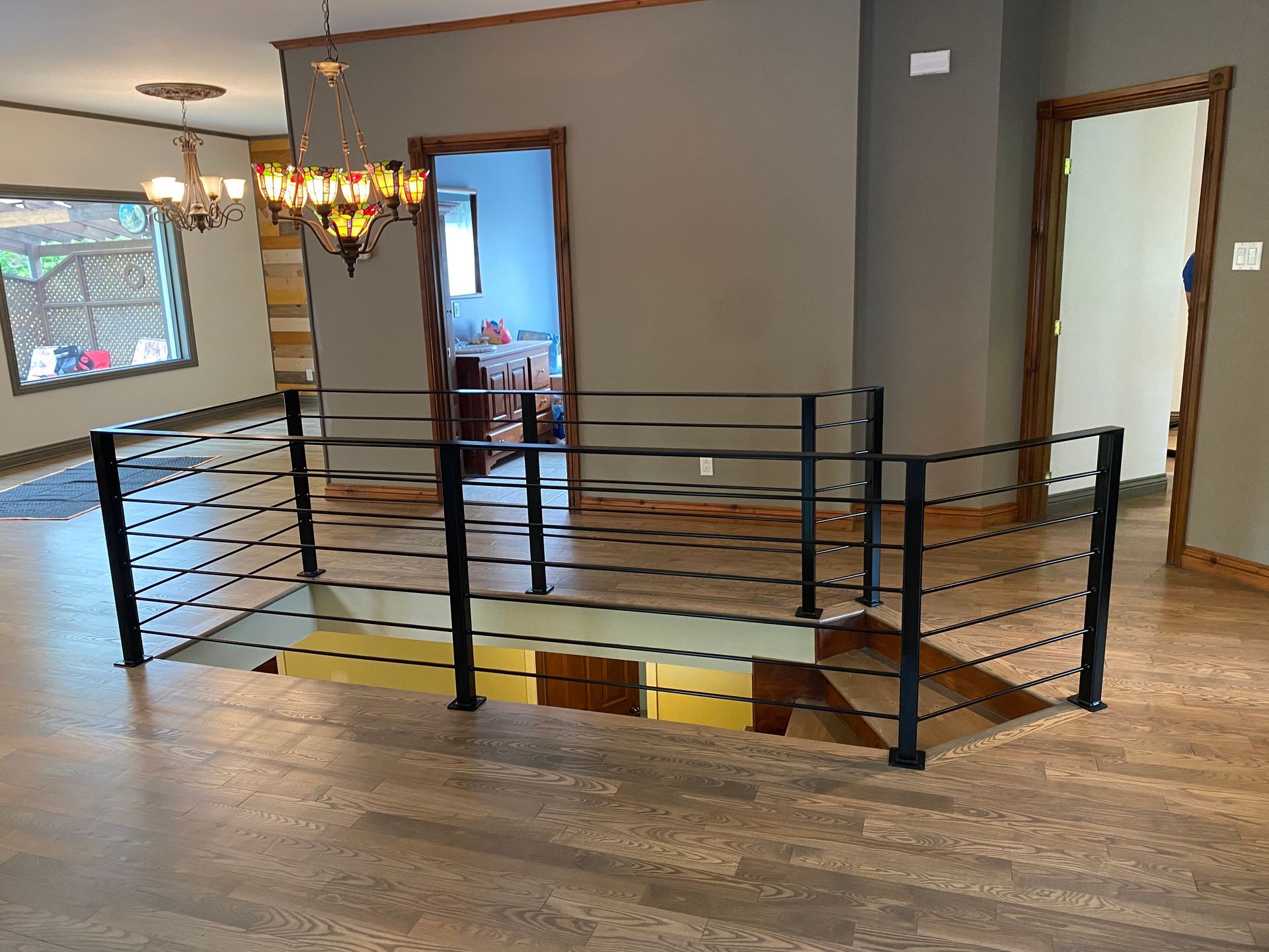 Vue intérieure d'une maison avec un escalier, une rampe noire et une porte ouverte.