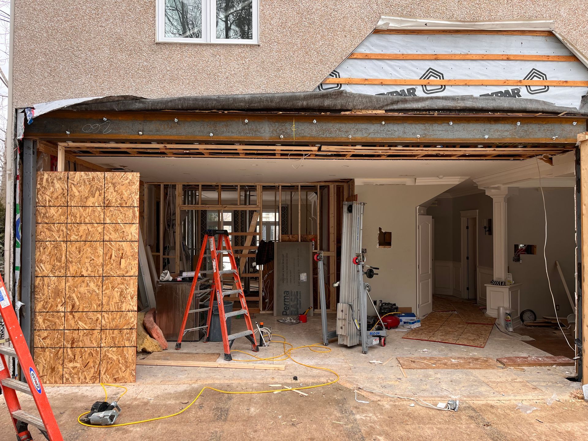 Maison en cours de rénovation ; mur extérieur enlevé, laissant apparaître l'intérieur avec la charpente, une échelle et des outils.
