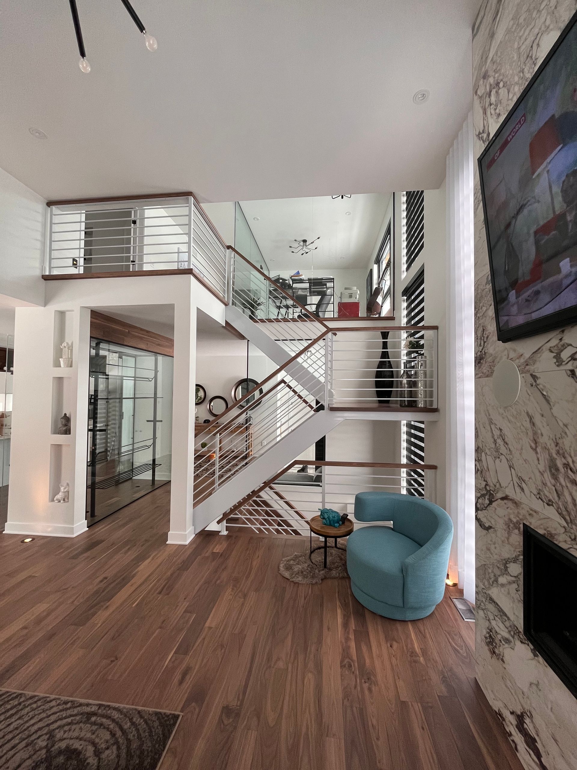 Intérieur d'une maison moderne avec parquet, escalier, fauteuil bleu et cheminée.
