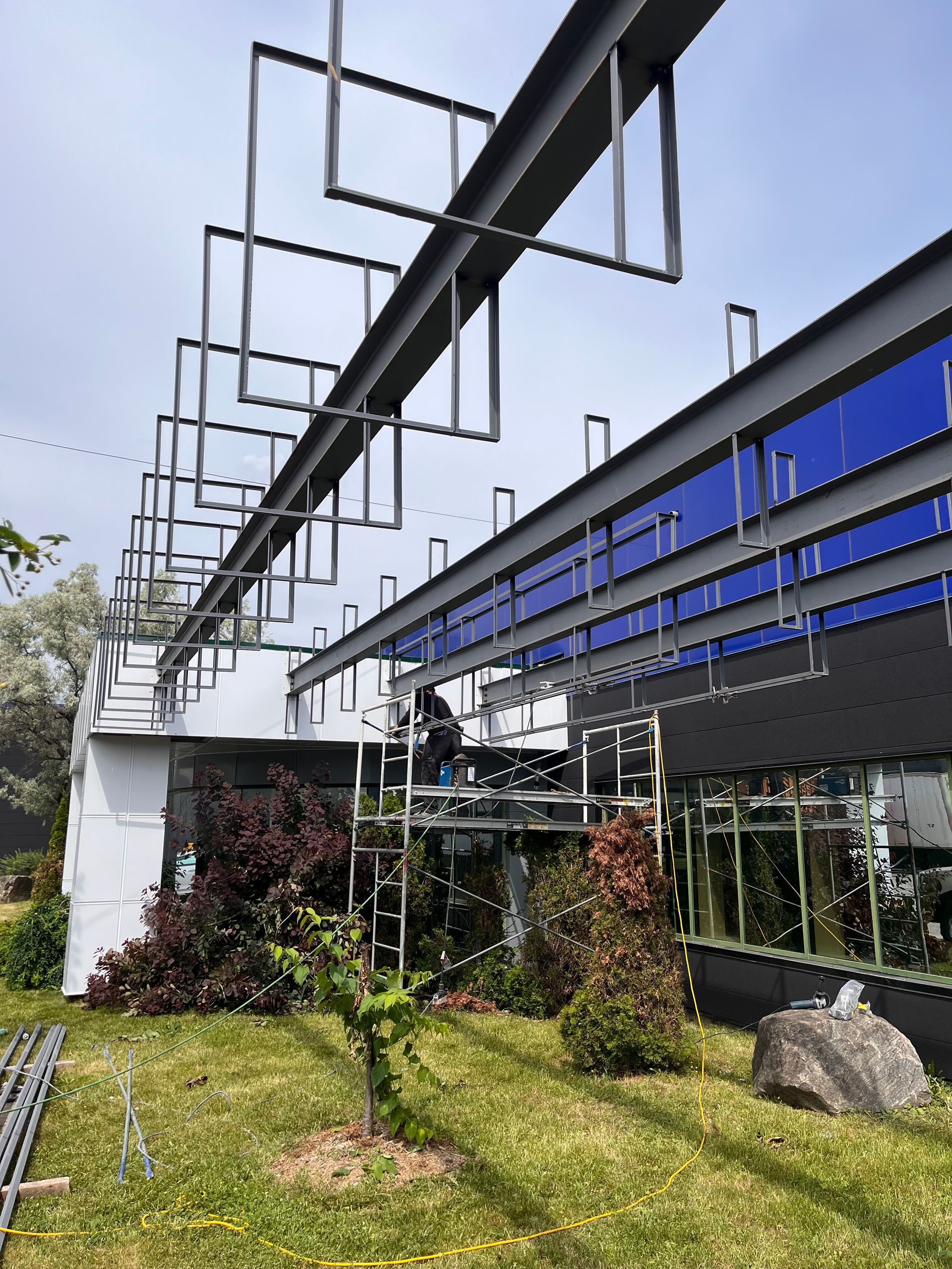 Poutres d'acier et formes géométriques s'étendant depuis un bâtiment moderne, ouvriers sur des échafaudages.