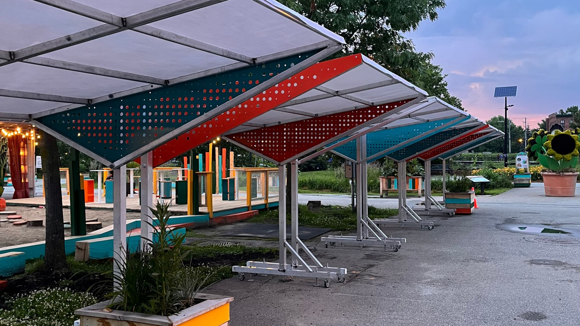 Structures d'ombrage colorées et angulaires, composées de panneaux rouges, turquoise et verts, dans un parc.