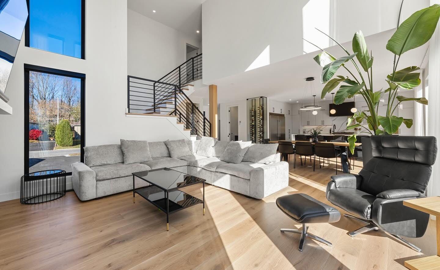Salon moderne avec parquet clair, canapé d'angle gris et fauteuil en cuir noir.