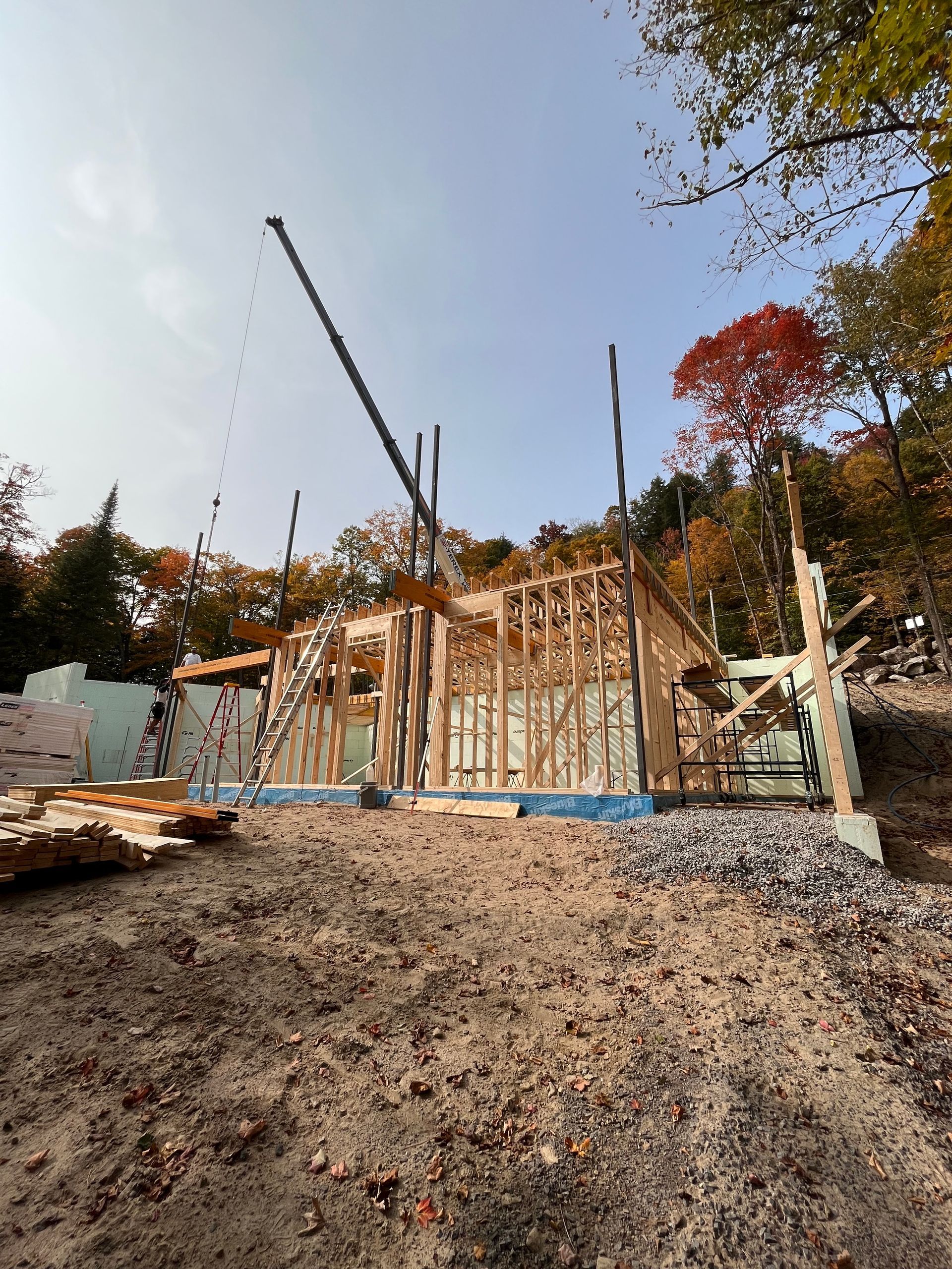 Construction d'une structure en bois, avec des montants apparents et une grue, sur fond d'arbres aux couleurs d'automne.
