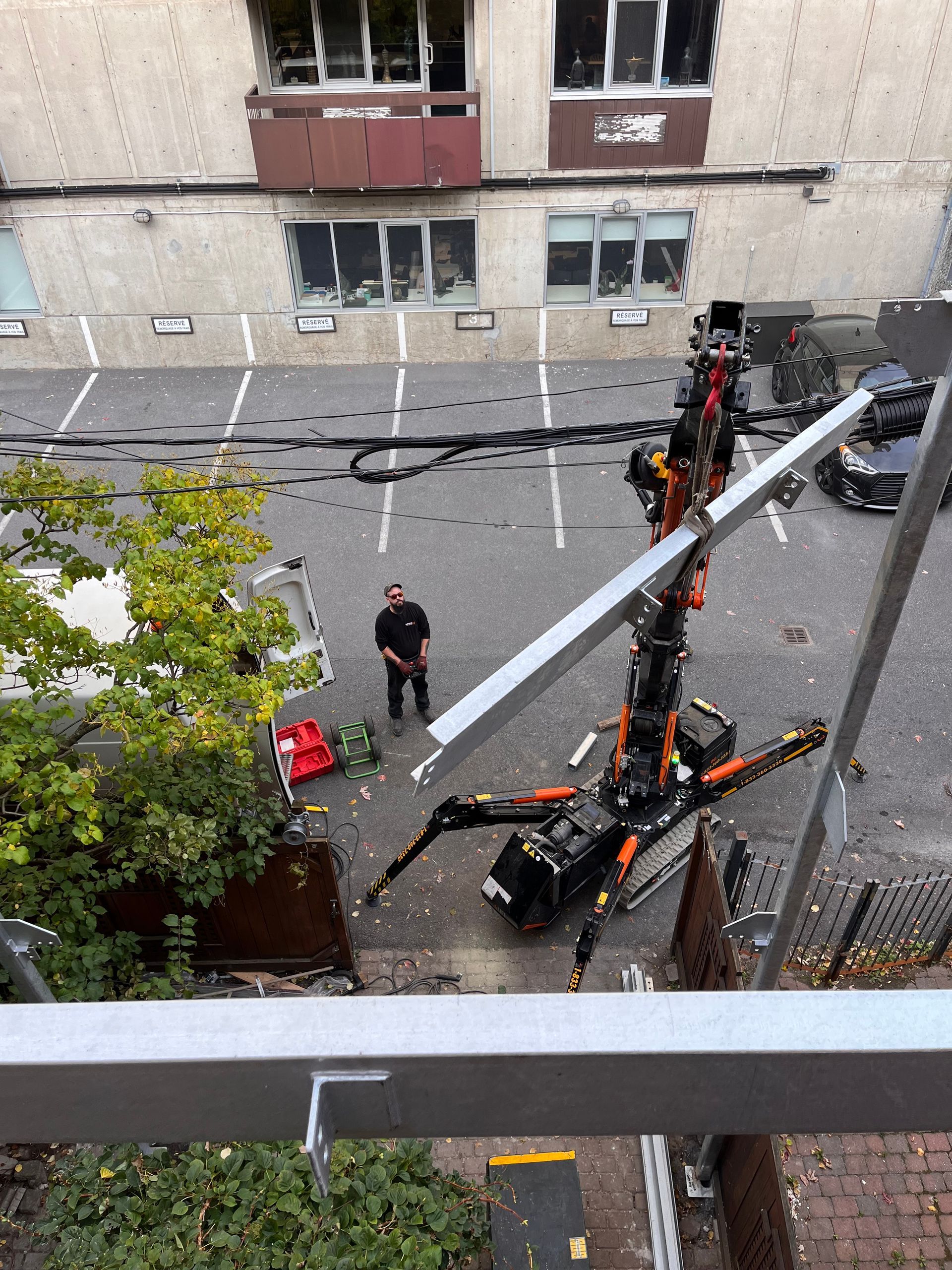 Un ouvrier observe une machine industrielle en forme d'araignée soulever une poutre métallique près d'un bâtiment.