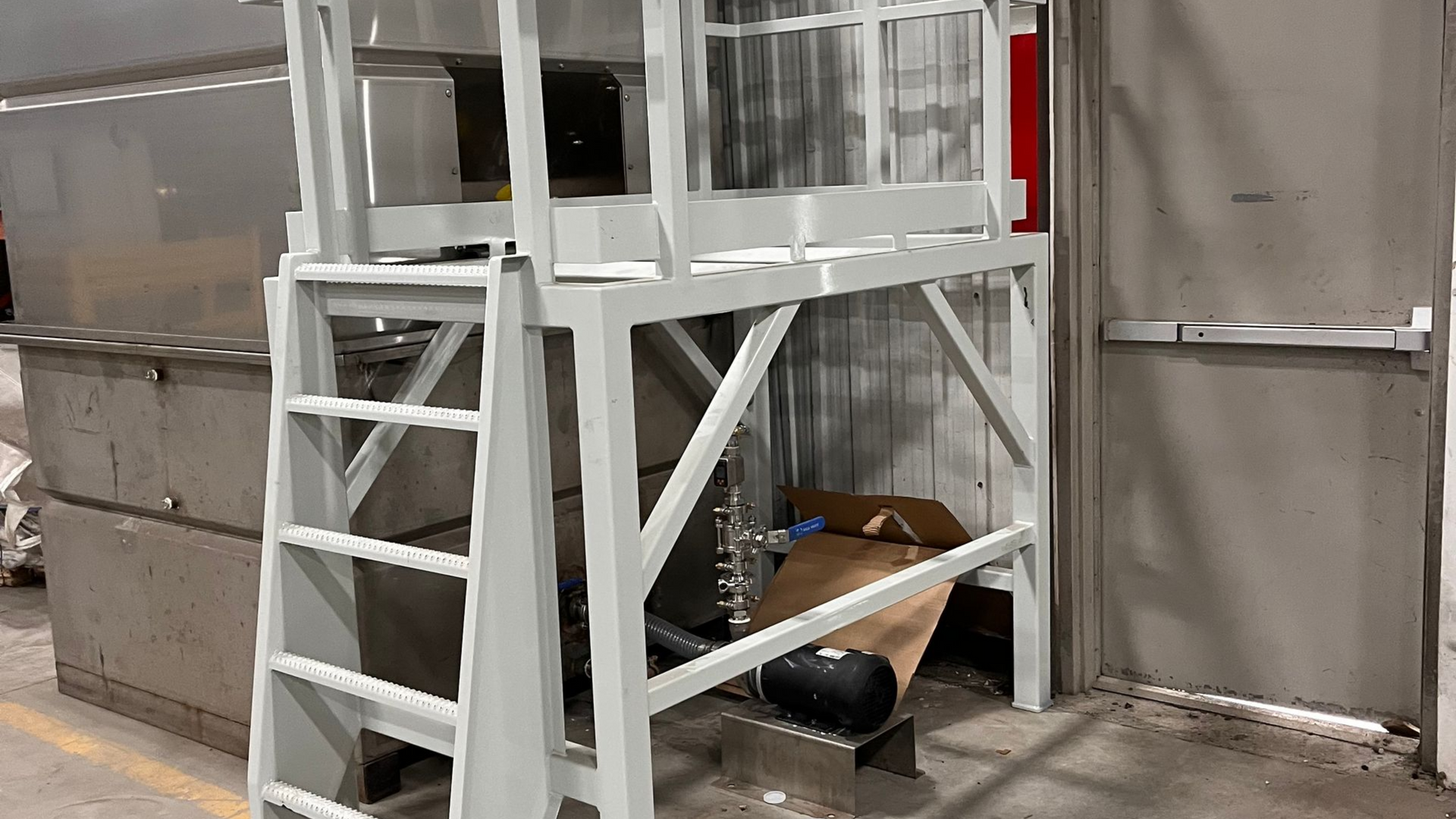 Plateforme industrielle en métal blanc avec échelle, adossée à un mur en béton.