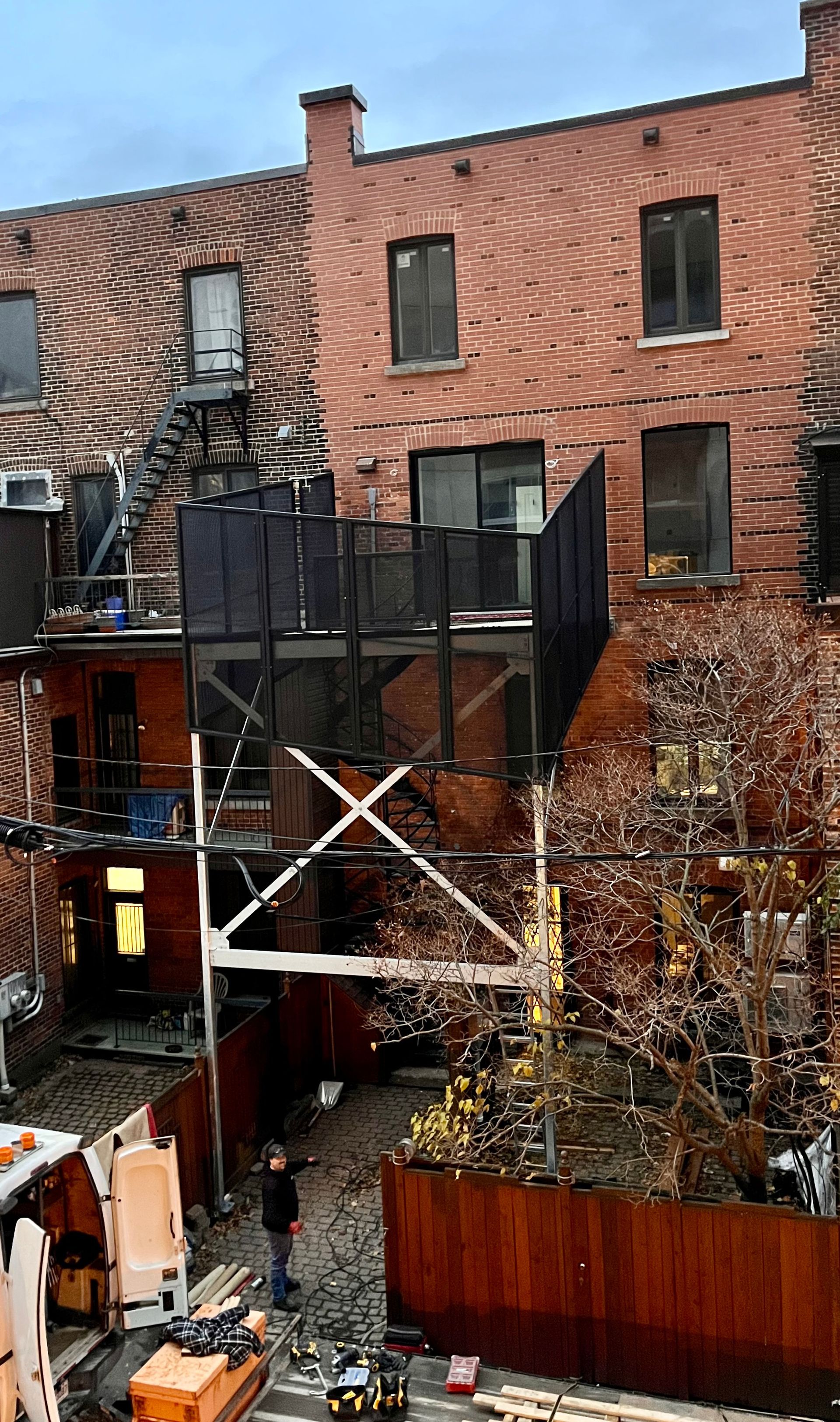 Bâtiments en briques, balcons en métal noir et échafaudages. Une personne se tient dans la cour.