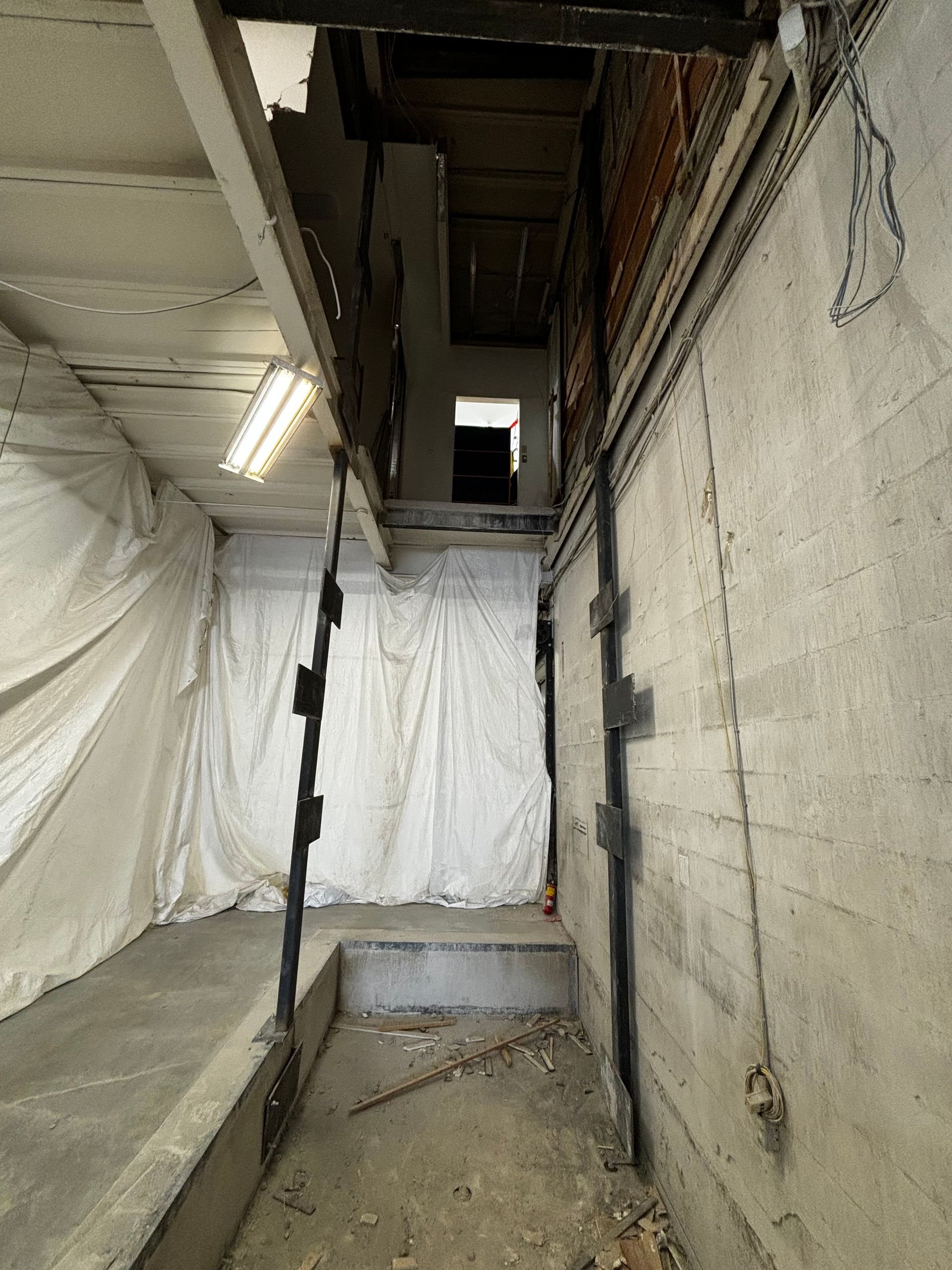 Intérieur du sous-sol avec briques et béton apparents. Un escalier mène à l'étage supérieur ; les supports sont visibles dans les murs.