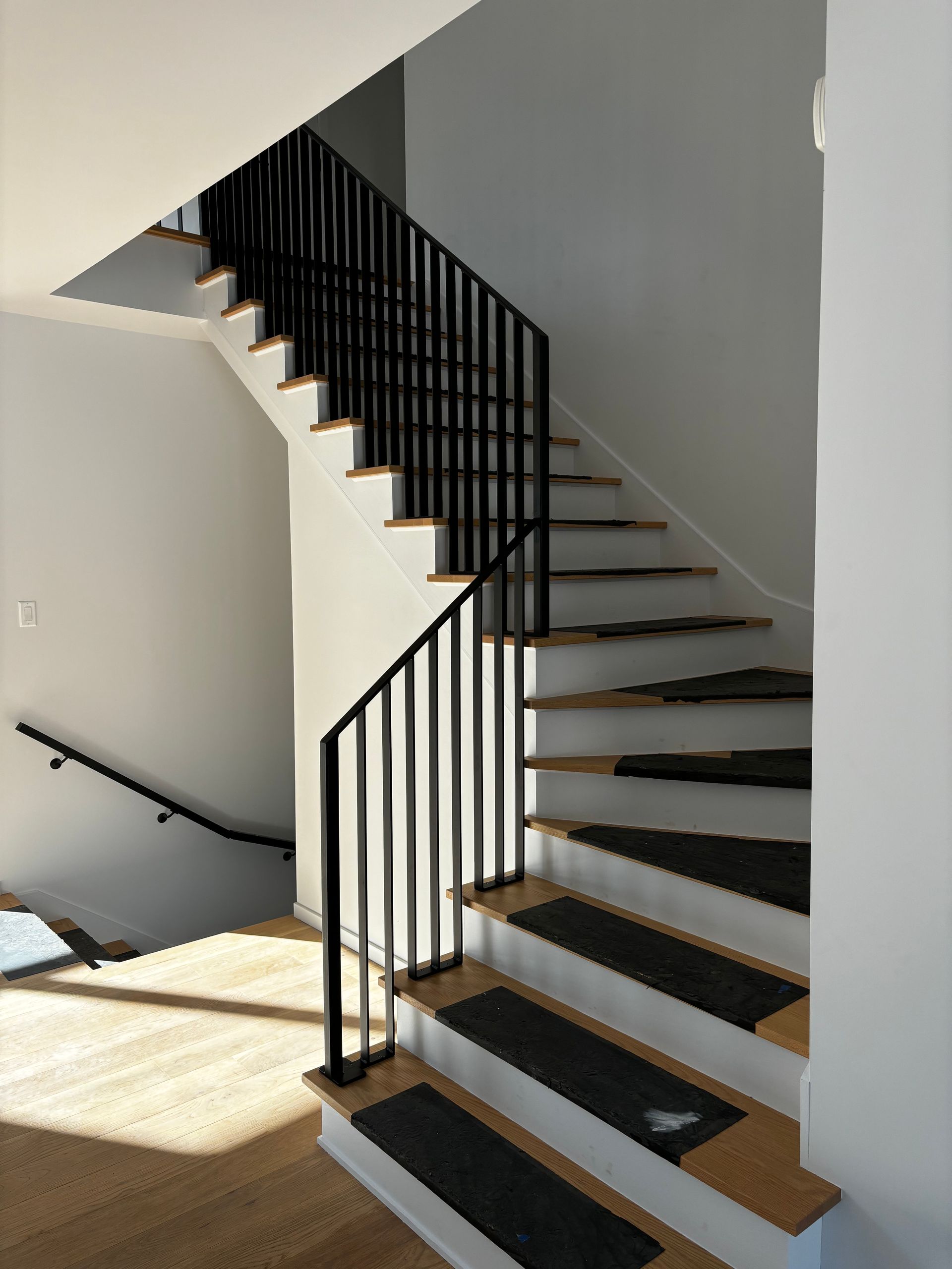 Escalier avec rampe en métal noir, marches en bois et murs de couleur claire.